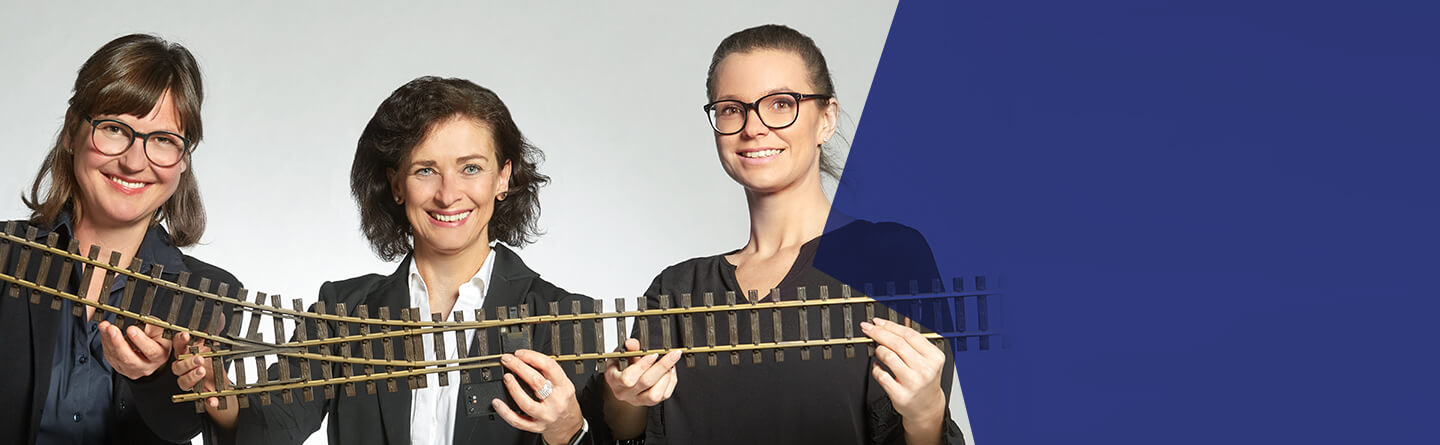 Header: Drei Damen aus dem Projektteam halten Modellbau-Schienen